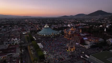 Aerial-view-around-the-illuminated-Basilica-of-Guadalupe,-dusk-in-Mexico---circling,-drone-shot