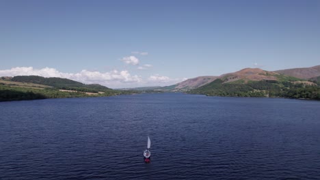 Slow-drone-shot-flying-forward-over-a-sail-boat-on-a-sunny-day,-Ullswater,-Lake-District,-Cumbria,-UK