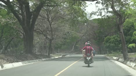 Two-men-riding-motorcycle-along-single-lane-road-with-helmets-on,-Following-behind-shot
