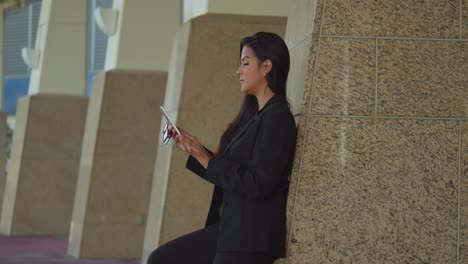 Young-latina-leans-on-a-wall-in-the-Caribbean-city-of-Trinidad,-Port-of-Spain-in-business-attire