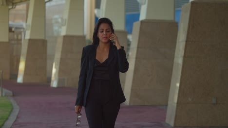 Mujer-Latina-Caminando-Y-Hablando-Por-Teléfono-En-Un-Ambiente-De-Ciudad-Vistiendo-Atuendo-De-Negocios
