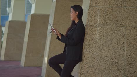 Hispanic-lady-holds-her-tablet-in-a-city-setting-in-business-attire-on-a-sunny-day