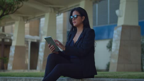 Young-woman-sits-on-the-steps-in-a-Caribbean-city-while-on-her-tablet-device-in-business-attire
