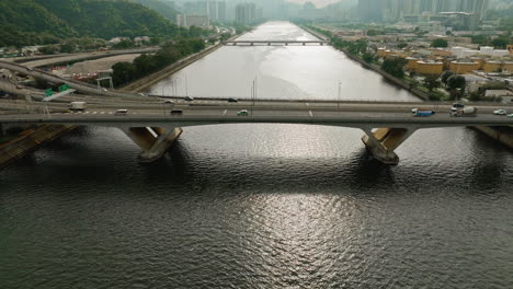 Tiro-De-Inclinación-Aérea-Coches-Conduciendo-En-La-Carretera-Sobre-Un-Amplio-Puente-Fluvial,-Hong-Kong
