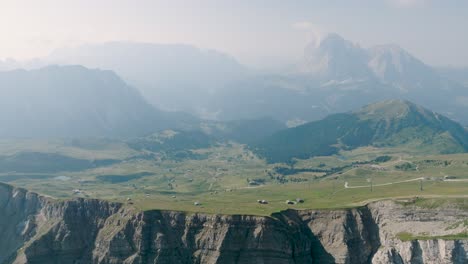 Drohnenflug-Zeigt-Die-Grünen-Bergwiesen-Mit-Einem-Kleinen-Dorf-Auf-Einer-Flachen-Ebene-In-Den-Dolomiten-In-Südtirol