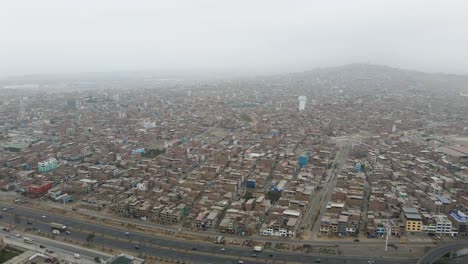 Drone-shot-of-massive-and-crowded-neighborhood-next-to-a-highway-in-Ventanilla-in-the-district-of-San-Juan-de-Miraflores