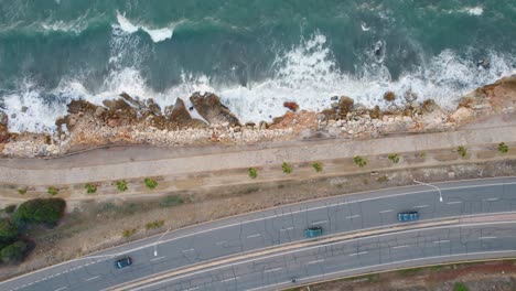-Lateral-drone-shot-above-coastal-road-and-seashore,-aiming-down-to-the-road,-with-cars-passing-by