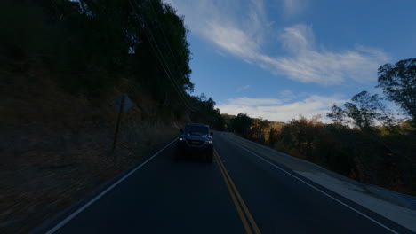 Fpv-drone-view-of-black-car-driving-fast-on-road-at-evening