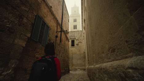 Mujer-Caminando-En-Una-Calle-Estrecha-Hacia-Una-Alta-Torre-De-Iglesia-En-Italia-En-4k