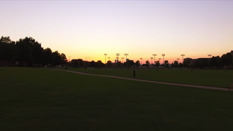 Low-aerial-dolly-forward-with-vibrant-sunset-of-floodlights-at-a-park