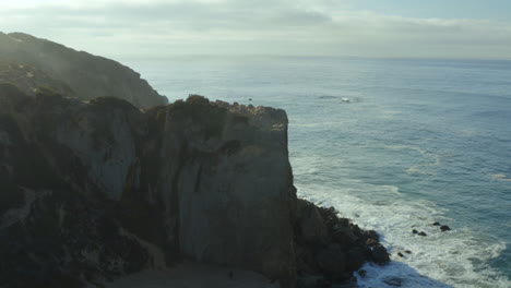 Aerial-establishing-shot-of-the-waves-crashing-against-the-rocks-at-the-beach
