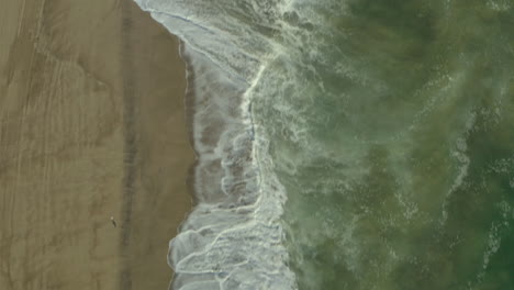 Aerial-dolly-shot-looking-down-on-the-waves-crashing-on-the-sandy-beach