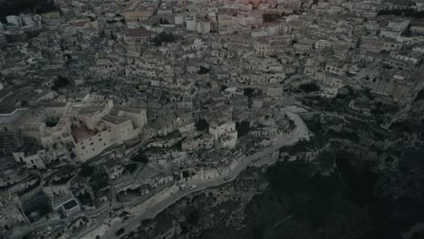 Drone-flying-backwards-with-the-camera-tilting-up-slowly-filming-the-old-white-city-of-Matera-at-sunset-in-4k