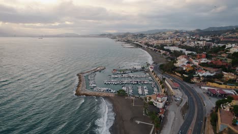 Aerial-forward-moving-drone-shot-over-El-Candado-beach-and-coastal-road-in-Malaga-Spain-with-view-on-seashore,-marina-and-beach-houses