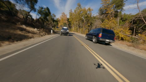 Fpv-drone-shot-of-black-car-driving-fast-on-road-at-morning