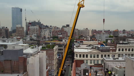 Aerial-View-of-Crane-Transporting-Load-Above-Workers-on-Rootopf-of-Residential-Building-in-Manhattan,-New-York-USA
