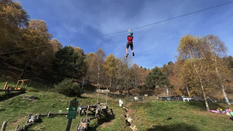 Children-have-fun-with-zip-line-at-rope-adventure-park,-forest-in-background-and-sky-for-copy-space