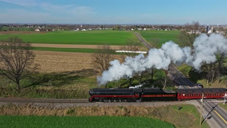Drone-Traveling-Parallel-View-of-a-Steam-Passenger-Train-Blowing-Lots-of-Smoke-and-Steam-on-a-Sunny-Fall-Day