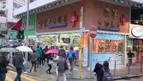 Chinese-pedestrians-walk-through-a-zebra-crossing-in-front-of-a-pharmacy-offering-and-selling-personal-care,-hygiene-products,-and-drugs-during-flu-season-in-Hong-Kong