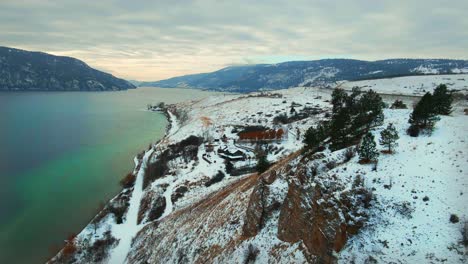 Aerial-View-of-Turquoise-Wood-Lake-in-Kelowna-with-Snow-Covered-Red-Cliffs-along-the-Shore