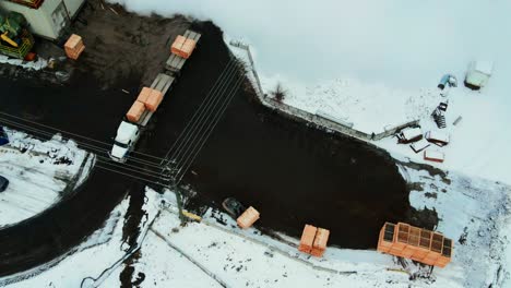 Aerial-overhead-shot-of-forklift-unloading-wooden-forms-from-white-semi-truck-in-winter-and-stacking-them-in-the-yard