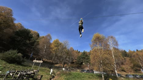 Little-girl-have-fun-with-zip-line-at-rope-adventure-park,-forest-in-background-and-sky-for-copy-space