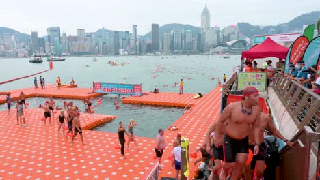 Teilnehmer-Und-Schwimmbegeisterte-überqueren-Die-Ziellinie-Während-Des-Jährlichen-Schwimmwettbewerbs-New-World-Harbour-Race,-Während-Die-Skyline-Von-Hongkong-Im-Hintergrund-Zu-Sehen-Ist