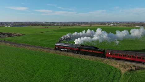 A-Drone-Parallel-to-Behind-View-of-a-Steam-Passenger-Train-Blowing-Lots-of-Smoke-and-Steam-on-a-Sunny-Fall-Day