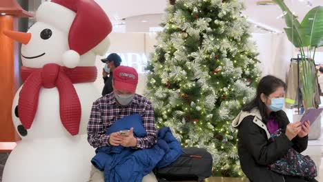 Shoppers-sit-on-a-bench-next-to-a-Christmas-tree-and-snowman-installation-at-a-shopping-mall-in-Hong-Kong