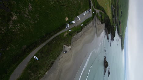 Sandy-beach-and-coastal-parking-in-New-Zealand,-aerial-drone-vertical-view