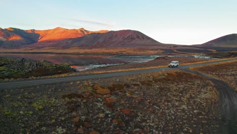 Camioneta-Blanca-Conduciendo-Por-La-Carretera-Del-Círculo-Dorado-En-Islandia-En-Un-Hermoso-Paisaje-Volcánico-Naranja-Rojo-Durante-La-Puesta-De-Sol