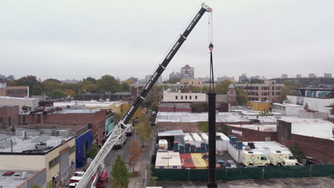 Drone-Shot-of-Crane-Holding-Metal-Support-For-Billboard-Above-Building-Rooftop
