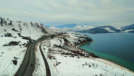 An-Aerial-Perspective-of-Snow-Covered-Landscape,-Traffic-on-Highway-97,-and-Turquoise-Wood-Lake