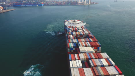 Riesiges-Containerschiff,-Das-Zum-Entladen-Von-Schleppern-Zum-Dock-Geschoben-Wird,-Mit-Der-Steinmetzbrücke-Und-Dem-Containerhafen-Im-Hintergrund-In-Hong-Kong