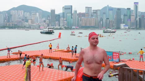 Die-Teilnehmer-überqueren-Die-Ziellinie-Während-Des-Jährlichen-Schwimmwettbewerbs-New-World-Harbour-Race,-Während-Die-Skyline-Von-Hongkong-Im-Hintergrund-Zu-Sehen-Ist