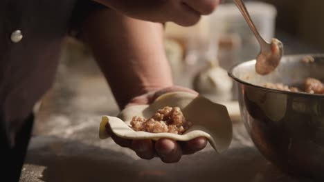 Adding-pork-meat-filling-to-dumplings,-closeup-on-chef-hands