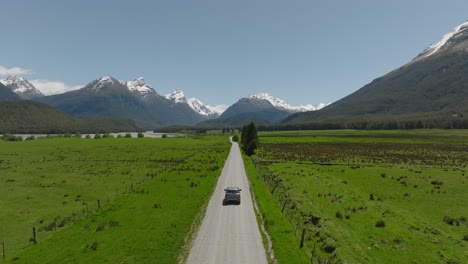 Car-driving-on-gravel-road-through-remote-green-grass-land-in-New-Zealand