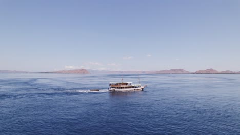 Tourist-Cruise-Boat-Traveling-in-Blue-Ocean-Nearby-Komodo-Island-Distant-Aerial-Orbiting