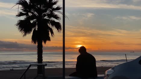 Silhouette-Man-Sitting-On-A-Bench-At-Sunset,-Then-Walks-Away,-In-Slow-Motion