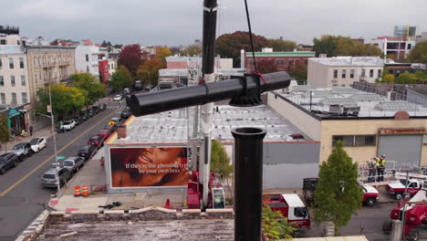 Aerial-of-Crane-Lifting-Catwalk-of-Billboard-Above-Support-Metal-Construction-and-Rooftop-of-Builings