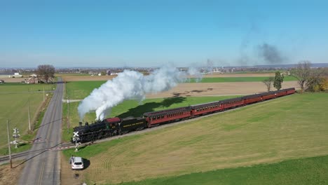 Drone-In-Front-of-View-of-a-Steam-Passenger-Train-Blowing-Lots-of-Smoke-and-Steam-on-a-Sunny-Fall-Day