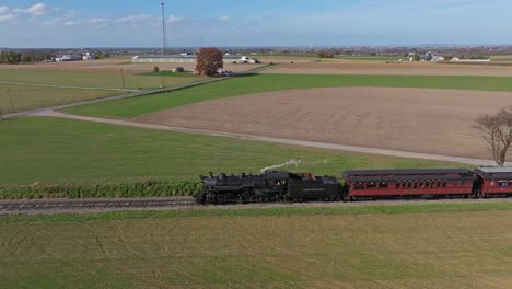 Aerial-Parallel-View-of-a-Steam-Passenger-Train-on-a-Single-Track-Thru-Farmlands-Approaching-a-Crossing-on-a-Sunny-Day