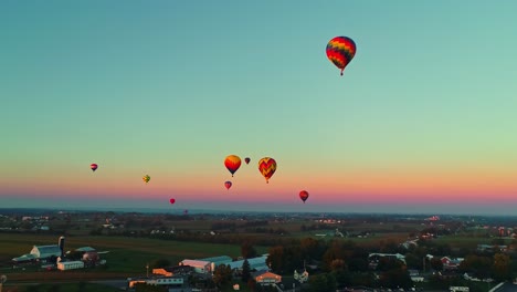 An-Aerial-View-of-Multiple-Hot-Air-Balloons-Rising-in-the-Late-Afternoon-During-a-Festival-With-Crowds-Watching,-on-a-Summer-Day