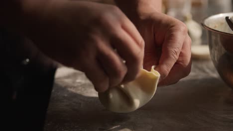 Chef-adding-fill-in-khinkali-dumplings-and-rolling-them-close,-closeup-on-hands