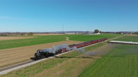 An-Aerial-Ahead-and-Parallel-View-of-a-Single-Rail-Road-Track-With-a-Steam-Train-Blowing-Smoke-on-a-Sunny-Fall-Day