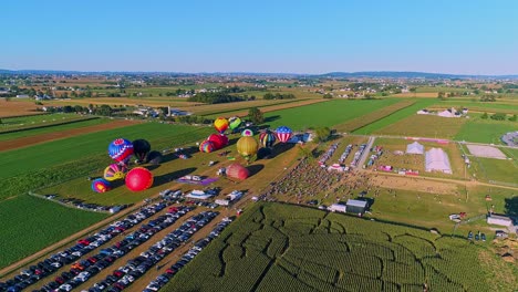 An-Aerial-View-of-Multiple-Hot-Air-Balloons-Rising-in-the-Late-Afternoon-During-a-Festival-With-Crowds-Watching,-on-a-Summer-Day