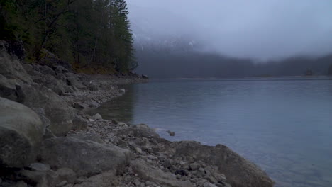 Lake-Eibsee-rocky-shoreline-and-misty-overcast-woodland-forest-mountains