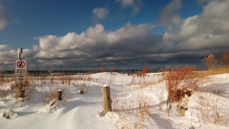 Exterior-panoramic-establishing-shot-of-a-sunny-snowy-Georgian-Bay-shoreline-with-water-in-the-distance