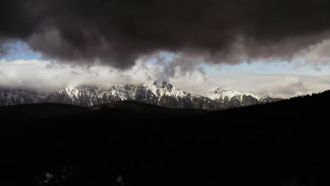 Moody-Aerial-Drone-Shot-of-Snow-Covered-Mountain-Range-with-Silhouette-Mountain-in-Foreground-and-Moody-Grey-Clouds