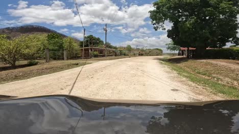 Grey-vehicle-advancing-on-dirt-road-in-rural-Costa-Rica-then-stops-near-farm,-Front-car-hood-shot